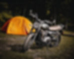 motor staat geparkeerd voor een tent in een bosrijke omgeving