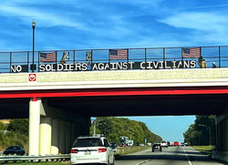 Sign on bridge attached to fence: Now Soldiers against Civilians