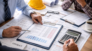 Construction project meeting reviewing costs and budget overrun risks with plans and financial documents