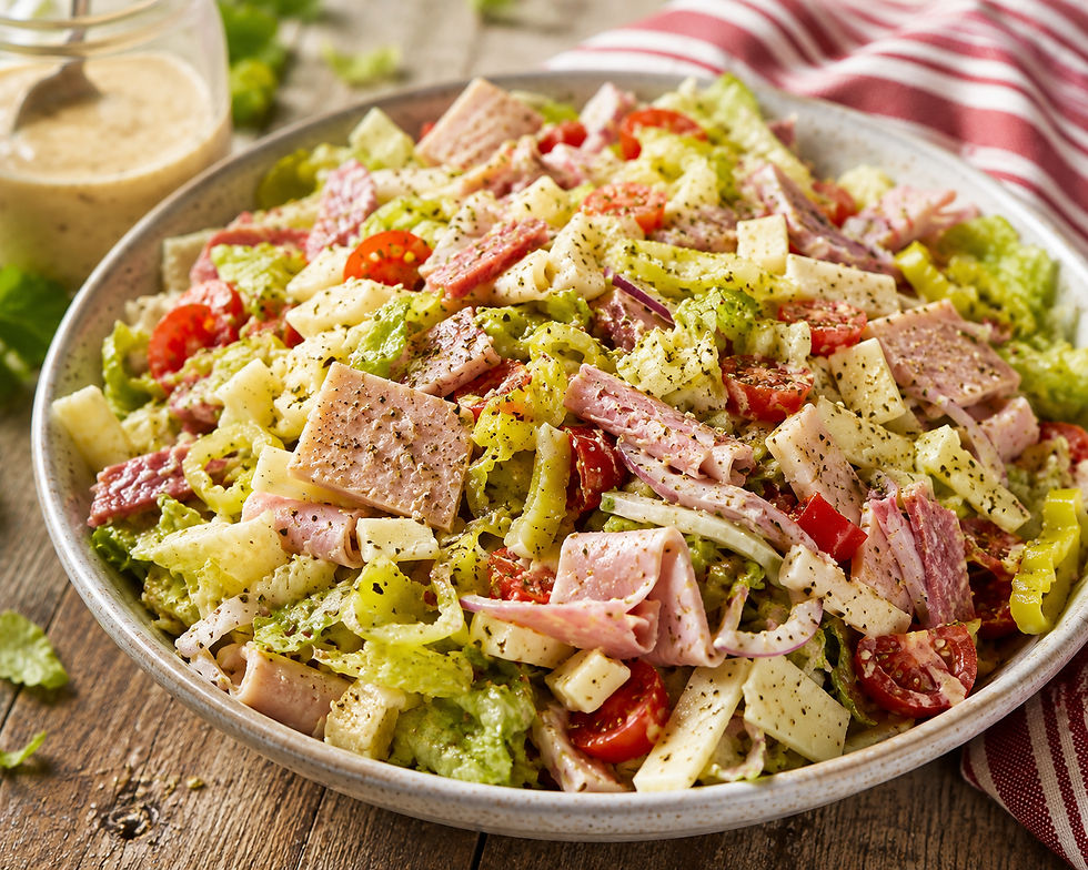 Italian Hoagie salad on a wooden table with a jar of salad dressing in the background.