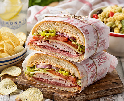 Italian hoagies wrapped in parchment stacked on top of each other on a wooden cutting board
