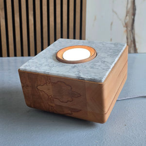 Quadratischer Bodenstrahler aus Holz und weiß-grau marmoriertem Naturstein mit zentraler runder LED-Lichtquelle; der Strahler steht auf einem strukturierten grauen Boden, daneben Holzlamellen und eine braun-weiß gemaserte Steinfläche.