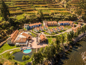 An aerial view of an exclusive luxury boutique resort with stone villas integrated into ancient agricultural terraces next to a river in Colca Valley.