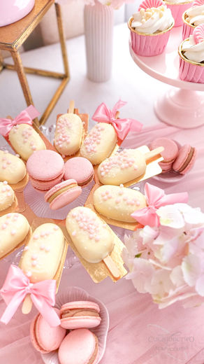 ukiernictwo Koszyczarski, Kalisz. Słodki stół przygotowany na komunię. Deserki oraz dekoracja w odcieniu różu oraz bieli. Mini deserki, kubeczki deserowe, monoporcje w kształcie kokardy, serniczkowe lody na patyku, makaroniki z różnym nadzieniem.
