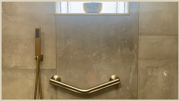 Accessible walk-in shower with large-format tiles, a wall-mounted teak bench, grab bar, and gold handheld showerhead. Designed by Design A Rose Interiors, a Black woman-owned interior design firm focused on aging-in-place solutions and inclusive luxury for Chicagoland clients