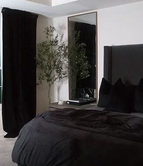 Luxury bedroom with a tall upholstered headboard, black-out drapery, full-length mirror, and layered black bedding. Designed by Design A Rose Interiors, a Black woman-owned interior design firm in Chicago specializing in calming, sensory-conscious spaces for affluent homeowners
