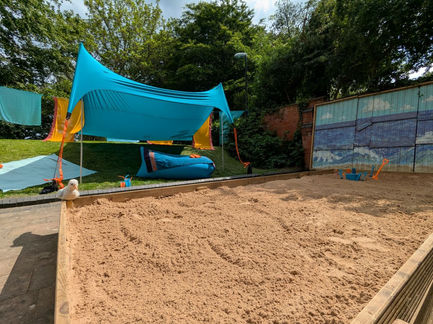 Sand pit, canopy, beach mural near natural trees.