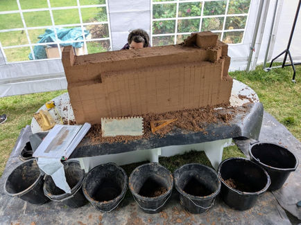 Sand sculptor barely seen behind the sculpture, tooks, buckets and plans.