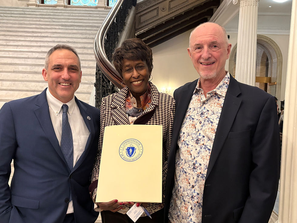 Josh, Carmen Fields, and spouse, standing in front of the grand staircase at the state house. Carmen holds her award.