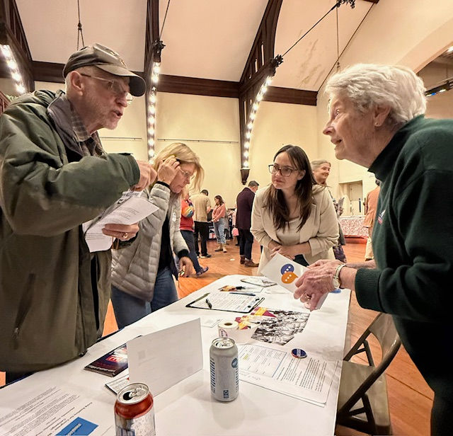 Group of people standing around a table in an auditorium talking