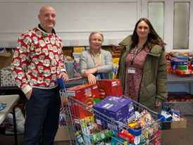 Three people stand around a shopping trolley full of food