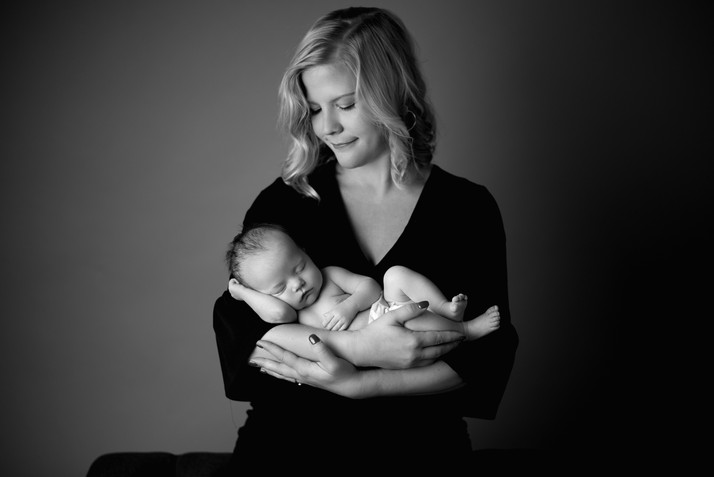 black and white portrait of a new mother smiling down at her sleeping newborn baby in her arms.