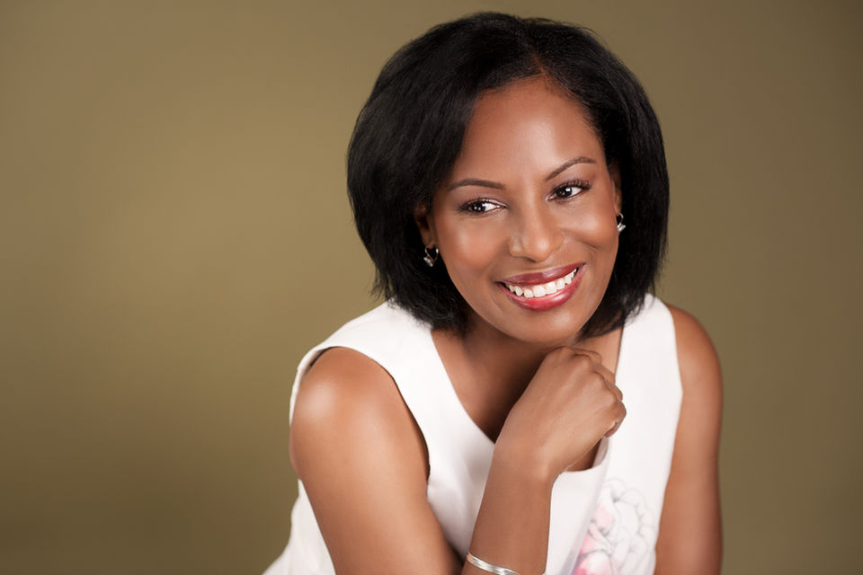 black woman rests her hand under her chin and poses with a soft and relaxed smile.