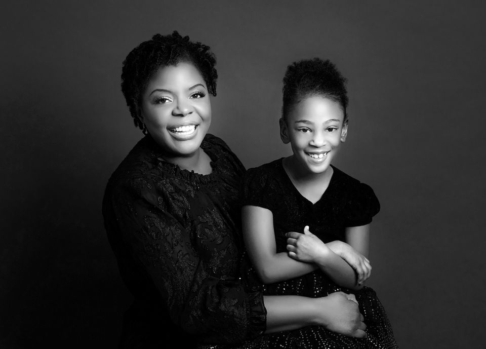 little girl sits on her mother's lap as they laugh and smile at the camera.