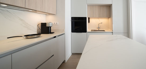 Cocina blanca minimalista con isla central y acabados en madera – Reforma en Barcelona