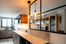 Cocina moderna, barra con encimera, separación de cristal, lámparas colgantes cálidas.