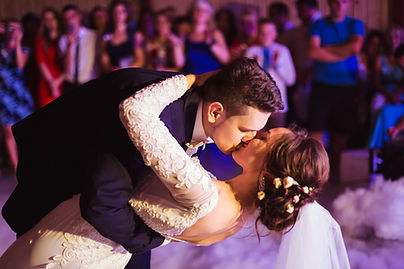 Groom kisses bride while dipping her during their first dance.
