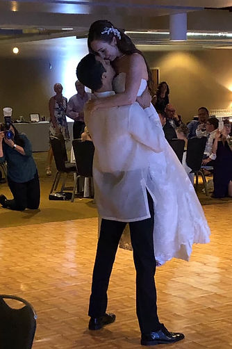 Wedding couple nose to nose as he lifts her up on the dance floor. Dancing as family looks on.