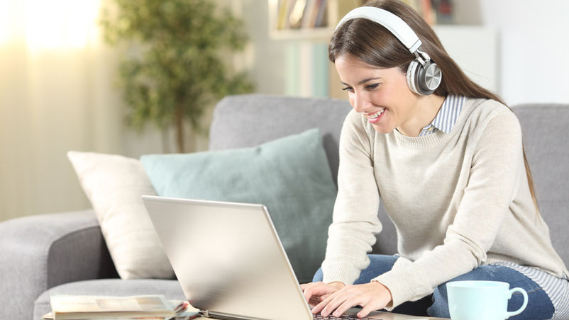 "Young woman with light gray sweeter in living room on a laptop searching for internet and TV service providers"