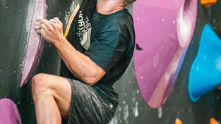 Boulderer klettert an einer bunten Boulderwand und konzentriert sich auf den nächsten Griff.