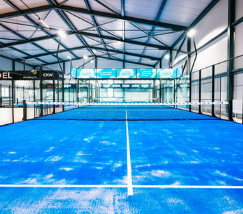 Leerer Indoor-Padelcourt mit blauen Spielflächen.