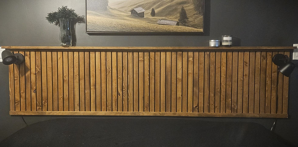 A lanscape view of the DIY wood slat headboard attatched to a dark grey wall. There is piece of artwork on the wall above it and a small vase with filigree places on the top ledge of headboard.