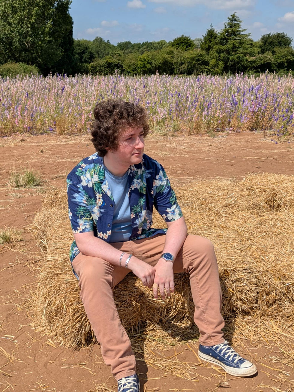 Photo of the counsellor sitting on a hay bale with confetti flowers behind him
