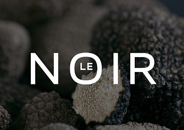 Gros plan sur des truffes noires avec le logo “LE NOIR” en lettres blanches au centre de l’image.