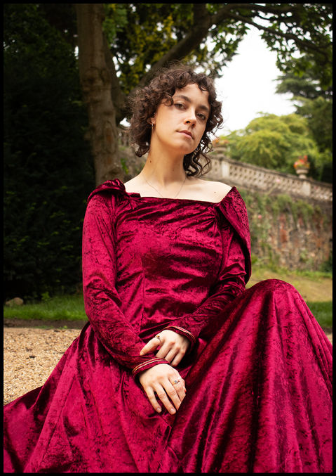 Indi in the red gown, sat with her legs on steps and both hands rested in her lap
