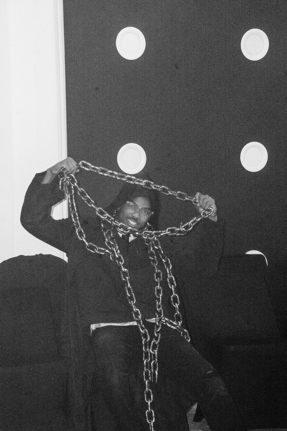 Man in black holding chains, two circles in background, black and white image.