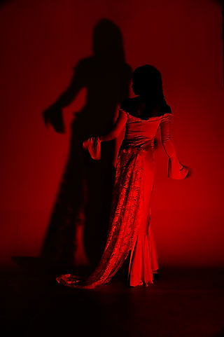 Two figures dance under red light, with a shadow on the wall.