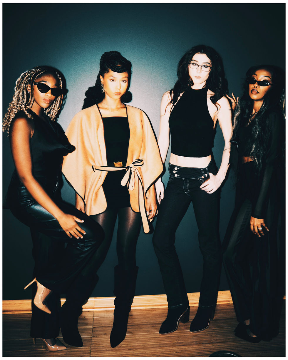 Four women posing for the camera with sunglasses and stylish outfits.