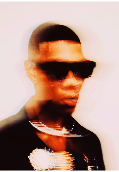 Stylish man wearing sunglasses and necklace posing with a blurred background.