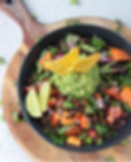 Black bowl of colorful salad with guacamole, tortilla chips, black beans, tomatoes, and lime on a wooden board