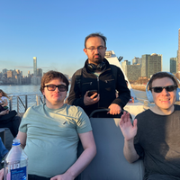 Three TSC members outside on the upper deck on a commuter ferry with NYC skyline and East River in the background.