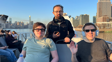 Three TSC members outside on the upper deck on a commuter ferry with NYC skyline and East River in the background.