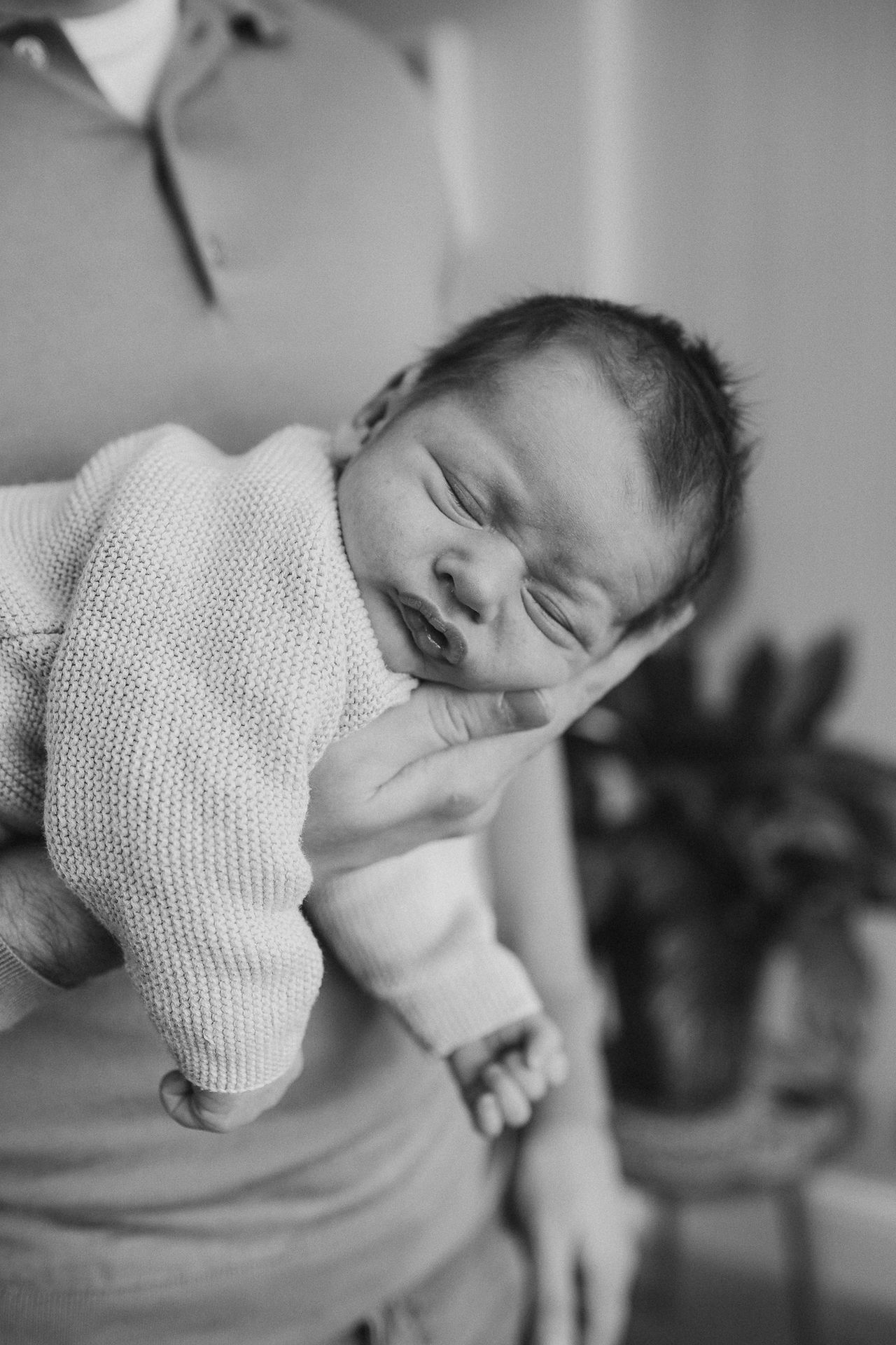Black and white image of newborn sleeping in parents hand taken during an in home newborn photoshoot in Chorlton.
