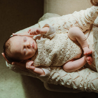 Baby lays sleeping peacefully on a mothers legs. Both are dressed in crochet clothing taken during a newborn photoshoot in Manchester.