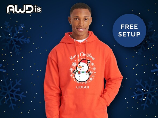 Young man standing looking at the camera wearing a orange hoodie promoting Christmas and branding/a logo on a hoody. Standing against a navy blue background with light 'snow' image