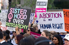Photo of protesters holding up signs reading, "Abortion is a Human Right".and "Sisterhood Over Patriarchy".