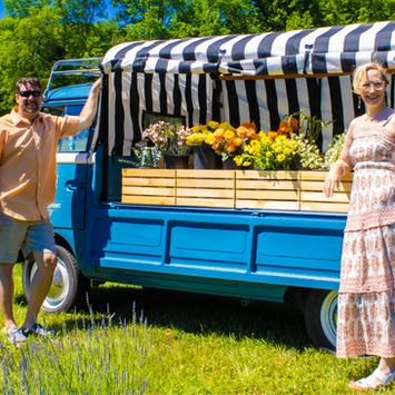 Couple standing by a blue 1962 VW flower truck with yellow blooms at Peacham Lavender Farm of Vermont.
