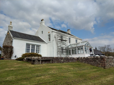 Painting the outside of a house with lots of grass and hedges framing the build.