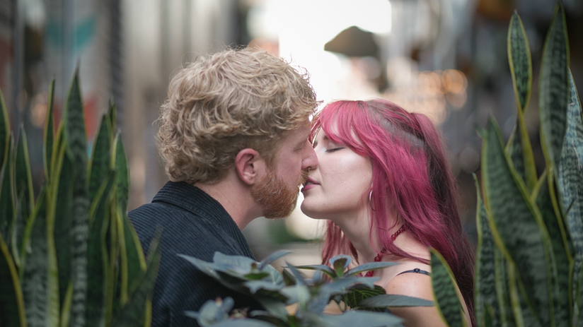 A photo peering through greenery while a couple shares a kiss