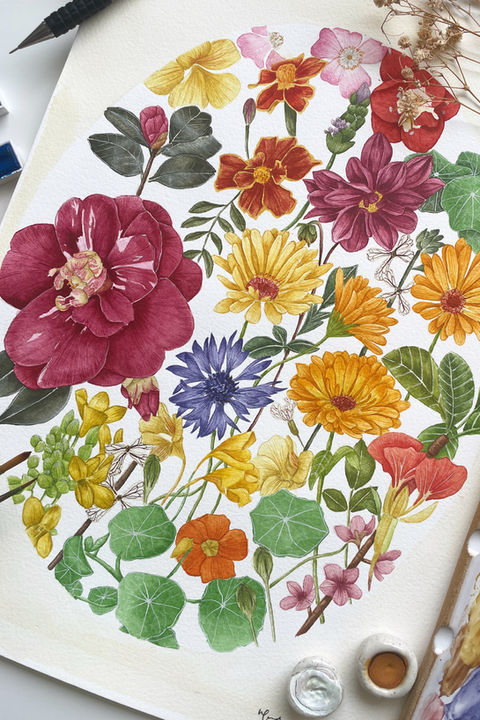 A vibrant watercolor painting featuring a variety of colorful flowers, including red, yellow, orange, blue, and pink blooms, with green leaves and delicate stems. The artwork is set on a white paper with a circular arrangement of flowers. Surrounding the painting are art supplies, including a black pencil, watercolor paints, a palette with mixed colors, and dried plant stems.