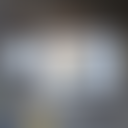 A small metal watercolor palette labeled “Poems About You” sits open on a wooden surface beside a sheet of watercolor swatches. The palette contains six earthy, muted colors. The swatch sheet shows neatly arranged square washes in soft, neutral tones—warm browns, ochres, greys, blues, and muted reds—demonstrating subtle variations in value, granulation, and transparency.