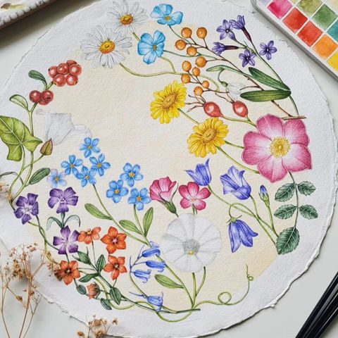 A vibrant watercolor painting featuring a circular arrangement of colorful flowers, including yellow daisies, blue forget-me-nots, pink roses, and orange blooms, with green leaves and red berries on textured beige paper. Surrounded by art supplies such as paintbrushes, watercolor palettes, and dried plants, this detailed floral artwork captures the beauty of nature and creativity.