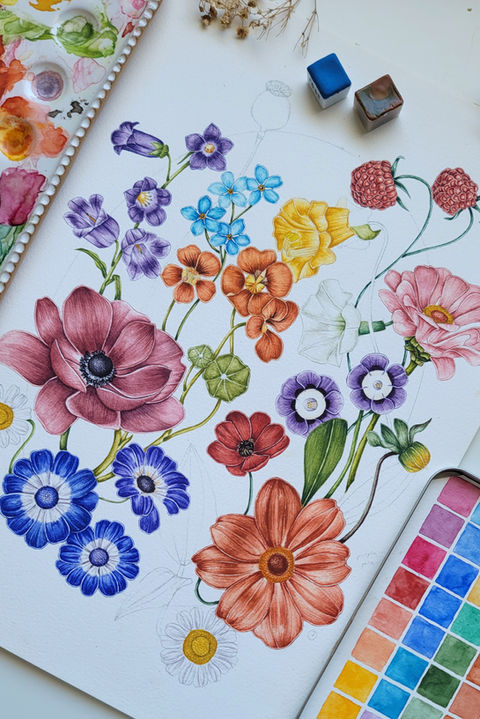 A vibrant watercolor painting featuring a colorful arrangement of flowers, including purple bell-shaped blooms, blue forget-me-nots, orange poppies, pink roses, and yellow daisies, with green leaves and red raspberries on white paper. Surrounded by art supplies such as paintbrushes, watercolor palettes with assorted colors, and dried plant stems, with a blue fabric visible at the bottom, showcasing the artistic process.