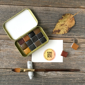 Poems About You handmade watercolour paints in a tin, featuring earthy purples, blues, browns, and greys, ideal for botanical painting, showing vibrant and muted pigment swatches.