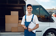 Delivery man with a clipboard standing in front of a white van with the side door open showing boxes.