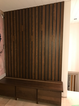 M&J Custom Cabinetry & Design custom dark wood slat background, a seat and storage drawers underneath.